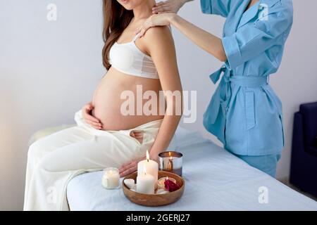 Wunderschöne asiatische Mama, die sich im Kosmetiksalon im Spa-Center Rücken- und Schultermassage gönnen konnte, mit Blick auf die entspannte Dame, die auf dem Bett saß und hatte Stockfoto