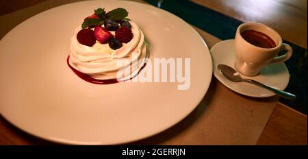 Pavlova-Kuchen mit frischen Erdbeeren, Blaubeeren und Minzblättern auf einem weißen Keramikplatte. Baiser-Dessert, Nahaufnahme Stockfoto