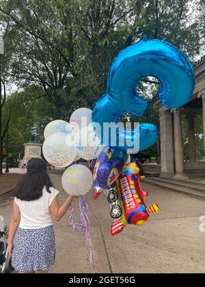 Frau geht mit einem Blumenstrauß Ballons in den Prospect Park, um eine Geburtstagsfeier für die drei Jahre zu feiern. Stockfoto