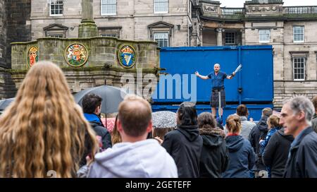 Royal Mile, Edinburgh, Schottland, Großbritannien, 21. August 2021. UK Wetter: Regen am Edinburgh Festival Fringe. Das trostlos nasse Wetter schreckt die Fringe-Massen oder die Straßenkünstler auf einem zurückgeschreckt Festival in diesem Sommer nicht ab. Ein Mann mit einem Kilt, der auf einer Leiter balanciert und mit Macheten jongliert Stockfoto