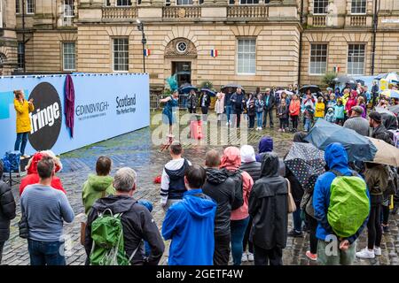 Royal Mile, Edinburgh, Schottland, Großbritannien, 21. August 2021. UK Wetter: Regen am Edinburgh Festival Fringe. Das trostlos nasse Wetter schreckt die Fringe-Massen oder die Straßenkünstler auf einem zurückgeschreckt Festival in diesem Sommer nicht ab. Eine Darstellerin auf dem Parliament Square mit einer Frau, die in Gebärdensprache dolmetscht Stockfoto