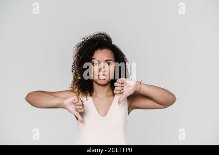 Die verärgerte Frau zeigte zwei Daumen nach unten, während sie im grauen Studio stand Stockfoto