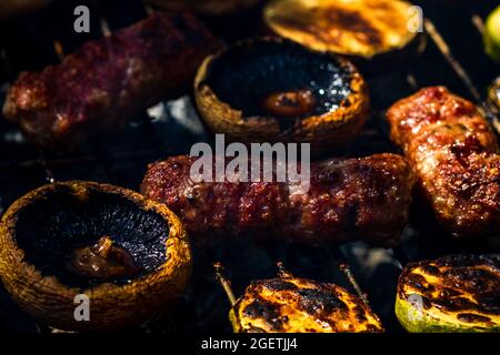 Nahaufnahme des Grillens von Fleischbrötchen, genannt Mici oder mititei mit Gemüse auf einem Grill Stockfoto