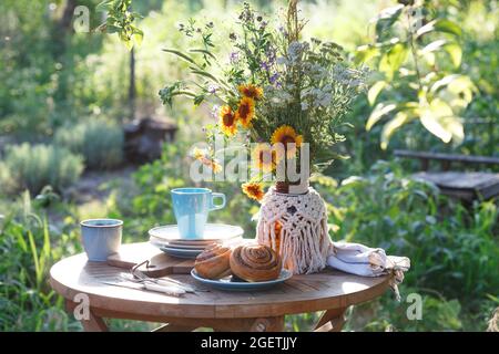 Garten- und Teeparty im Landhausstil. Stillleben - Zimtrollen, Tassen, Geschirr und eine Vase mit Wildblumen Stockfoto