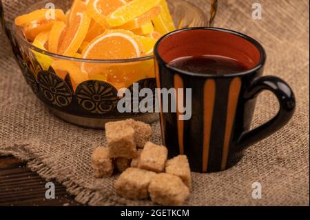 Bunte, geformte Marmeladenscheiben in einer Glasvase, Stücke braunen Rohrzuckers und eine Tasse Kaffee, Nahaufnahme, selektiver Fokus Stockfoto
