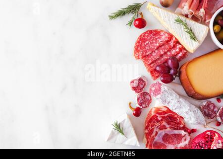 Auswahl an Käse- und Fleischgerichten. Seitenrand oben auf weißem Marmorhintergrund mit Kopierfläche. Stockfoto