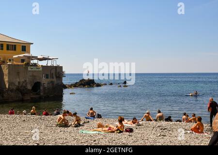 Menschen Sonnenbaden am Kiesstrand des alten Fischerdorfes im Sommer, Boccadasse, Genua, Ligurien, Italien Stockfoto