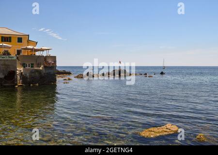 Blick auf die Küste des Fischerdorfes mit Felsen und einem Terrassenrestaurant im Hintergrund, Boccadasse, Genua, Ligurien, Italien Stockfoto