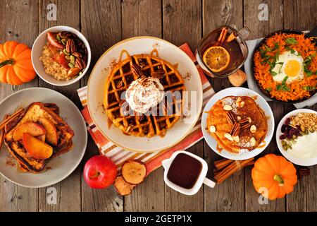 Herbstfrühstück oder Brunch am Buffettisch vor dunklem Holz. Kürbisgewürz, Waffeln, Pfannkuchen, französischer Apfel-Toast, Haferbrei, Eierpfanne Stockfoto