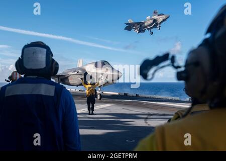 Uss America, Guam. August 2021. Besatzungen des US-Marine Corps beobachten, wie F-35B Lightning II Stealth-Kampfflugzeuge, die an das Marine Fighter Attack Squadron 211 angeschlossen sind, während der Einsätze am 20. August 2021 in der philippinischen See auf dem Flugdeck des amphibischen Angriffsschiffes USS America landen. Quelle: Planetpix/Alamy Live News Stockfoto