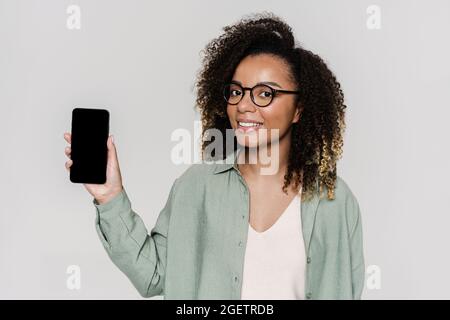 Eine lächelnde Frau mit dem Telefonbildschirm drehte sich im Studio zu einer Kamera Stockfoto
