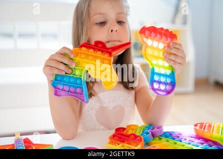 Kleines Mädchen, Kind, Kind spielt mit bunten Pop es Kinderzimmer, Schlafzimmer.Funny trendy Silikon Antistress bunte sensorische Push-Spielzeug popit.Flapping Fi Stockfoto