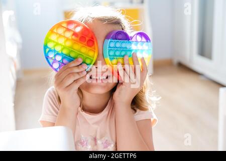 Kleines Mädchen, Kind, Kind spielt mit bunten Pop es Kinderzimmer, Schlafzimmer.Funny trendy Silikon Antistress bunte sensorische Push-Spielzeug popit.Flapping Fi Stockfoto