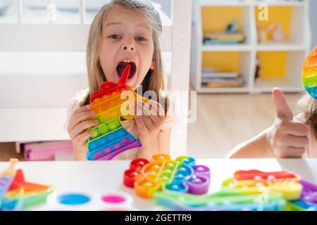 Kleines Mädchen, Kind, Kind spielt mit bunten Pop es Kinderzimmer, Schlafzimmer.Funny trendy Silikon Antistress bunte sensorische Push-Spielzeug popit.Flapping Fi Stockfoto