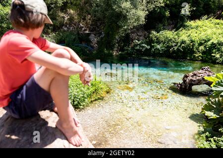 Junge, der auf einem Felsen sitzt und auf das Blaue Auge blickt, die Syri-i-Kalter-Karstquelle, den Bistrica-Fluss, in der Nähe von Saranda, Qark Vlora, Albanien Stockfoto