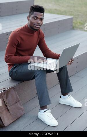 Junger erfolgreicher afrikanischer Geschäftsmann mit Laptop im städtischen Umfeld Stockfoto