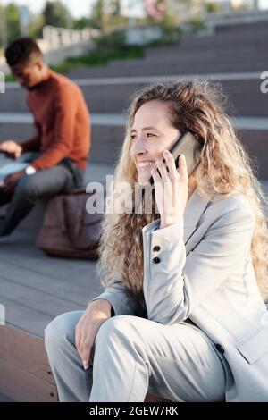 Glückliche junge Frau, die auf dem Smartphone gegen einen afrikanischen Geschäftsmann spricht Stockfoto