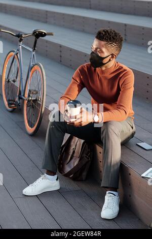 Junger, erholsamer Geschäftsmann mit einem Getränk, der während der Pause auf der Treppe sitzt Stockfoto