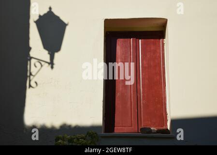 Alte rustikale Hausfassade mit einer Holztür und der Silhouette einer Straßenlaterne auf der weißgetünchten Wand in Anafiotika, Athen, Griechenland. Stockfoto