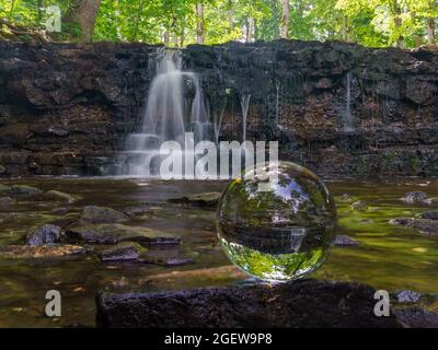 Der Wasserfall wurde im Sommer mit einer langen Belichtung fotografiert, die das Wasser verschwimmt, Bäume mit grünen Blättern sind im Hintergrund zu sehen. Stockfoto