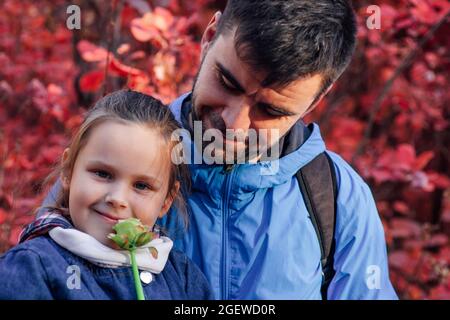 Close up glücklich Familie Konzept. Happy man in blauer Jacke Blick auf hübsches Mädchen hält Blume auf Herbst Wald Hintergrund Stockfoto