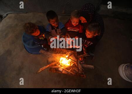 Eine Mutter und Kinder zünden ein Feuer in ihrem Haus an, um sich wegen des kalten Wetters warm zu halten. Gaza-Stadt. Stockfoto