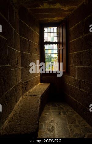 Ein Raum aus dunklem Stein mit einem Buntglasfenster im berühmten Schloss von Fougeres in Frankreich Stockfoto