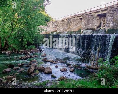 Schöner Blick auf eine Steinbrücke über einen kleinen Wasserfall inmitten von Vegetation Stockfoto