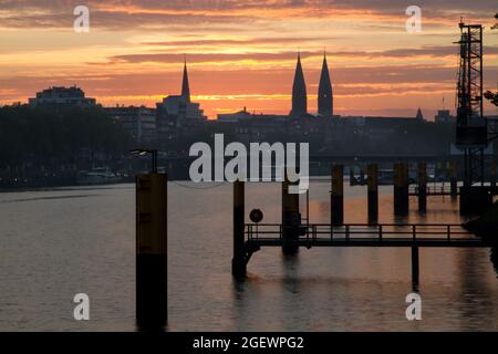 Schöner Sonnenaufgang mit dramatischem Himmel an der Weser in Bremen, Deutschland mit Kirchtürmen im Stadtbild Stockfoto