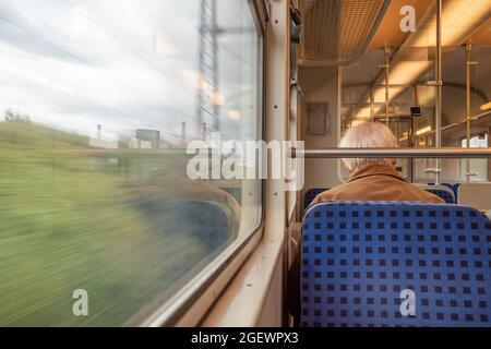 Innenansicht und ausgewählte Fokusansicht auf der Rückseite eines älteren männlichen Passagiers mit Gesichtsschutzmaske und Skinhead, der in der Straßenbahn oder im Zug in Deutschland sitzt. Stockfoto