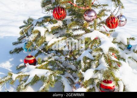 Grüner festlicher kleiner Weihnachtsbaum, der mit Spielzeug und Perlen im Schnee geschmückt ist. Stockfoto