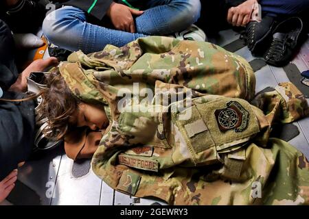 Ein afghanisches Kind schläft während eines Evakuierungsfluges aus Kabul, Afghanistan, am 15. August 2021 auf dem Frachtboden einer C-17 Globemaster III der US-Luftwaffe, die durch die Uniform des C-17-Ladermeisters warm gehalten wird. Das Air Mobility Command, das eine Flotte von Air National Guard, Air Force Reserve und Active Duty C-17 betreibt, hat zur Unterstützung des Verteidigungsministeriums Truppen ins Theater gebracht, um die sichere Ausreise und Umsiedlung von US-Bürgern, Empfängern von Sondereinreisevisa und gefährdeten afghanischen Bevölkerungen aus Afghanistan zu erleichtern. Quelle: United States Air Force via CNP /MediaPunch Stockfoto