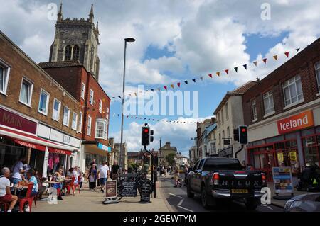 Die geschäftige High Street in Cromer im Sommer mit dem alten anglikanischen Kirchturm im Hintergrund Stockfoto