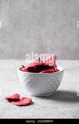 Pflanzliche Rote Beete-Chips in grauer Schale auf grauem Hintergrund. Veganer Snack. Nahaufnahme. Vertikales Format. Stockfoto