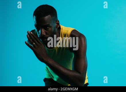 Nahaufnahme eines afroamerikanischen Athleten, der vor blauem Hintergrund sprintet Stockfoto