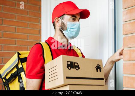 Der Lieferer trägt eine Gesichtsmaske und klingelt an der Haustürklingel, um das Paket zu liefern Stockfoto