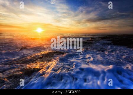 Sogar die Oberfläche der pazifischen Ozeanwellen reflektiert die heiße aufgehende Sonne über dem Meereshorizont vor den nördlichen Stränden von Sydney. Stockfoto