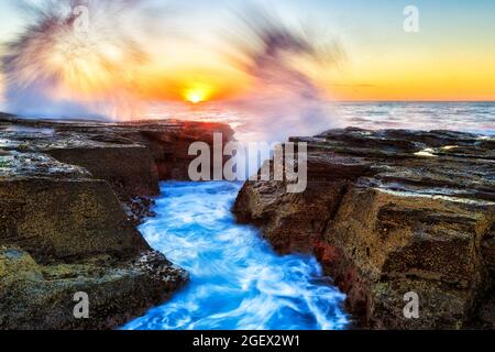 Hohe Wellen schlagen bei Sonnenaufgang über Sandsteinfelsen an den nördlichen Stränden Sydneys - malerische Pazifikküste. Stockfoto