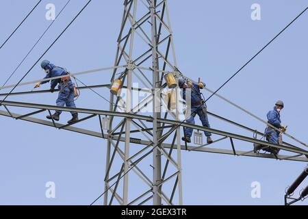 Industriekletterer Mast Saiten mit Helm und Schutzkleidung ist mit einem Seil gesichert gelöscht ein Power-Pole mit einer grauen Farbe. Stockfoto