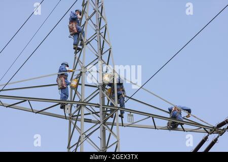 Industriekletterer Mast Saiten mit Helm und Schutzkleidung ist mit einem Seil gesichert gelöscht ein Power-Pole mit einer grauen Farbe. Stockfoto