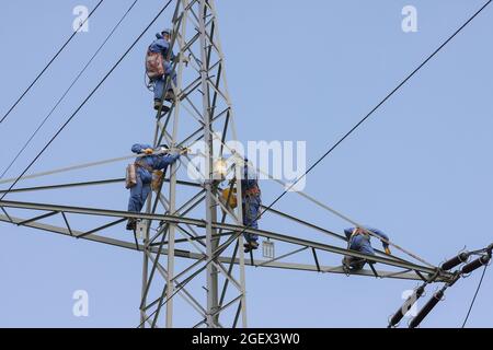 Industriekletterer Mast Saiten mit Helm und Schutzkleidung ist mit einem Seil gesichert gelöscht ein Power-Pole mit einer grauen Farbe. Stockfoto