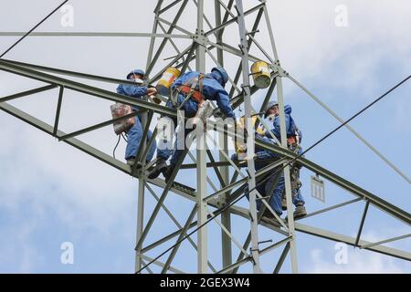 Industriekletterer Mast Saiten mit Helm und Schutzkleidung ist mit einem Seil gesichert gelöscht ein Power-Pole mit einer grauen Farbe. Stockfoto