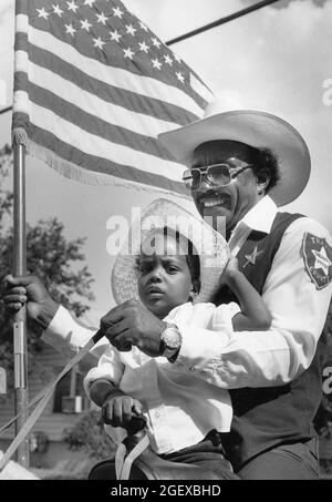 Austin Texas USA, um Juni 1993: Schwarzer Großvater mit amerikanischer Flagge und Enkel reiten während der Junienth-Parade zusammen zu Pferd. ©Bob Daemmrich Stockfoto