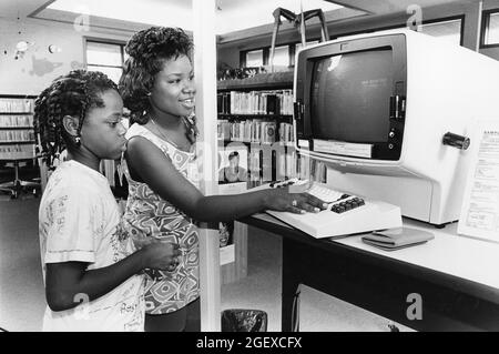 Austin, Texas, USA, um 1993: Schwarzes Teenager-Mädchen mit Sommerjob in der öffentlichen Bibliothek hilft Kindern, den elektronischen Kartenkatalog zu nutzen. Bibliothek in Austin, Texas. Modell Freigegeben. ©Bob Daemmrich Stockfoto