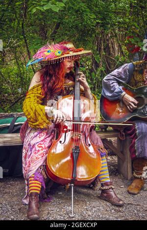 Mai 15 2011 Muskogee USA Frau im Zigeunerkostüm mit Schnurrbart spielt Cello auf der Bank vor Bäumen Stockfoto