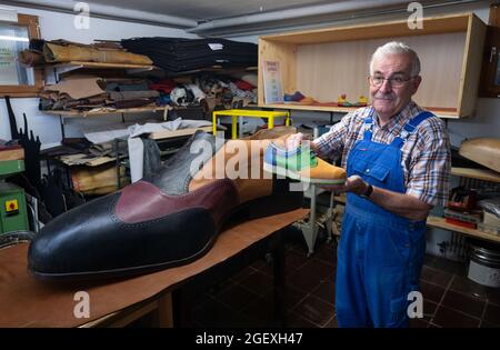 19. August 2021, Baden-Württemberg, Münsingen: Schuhmachermeister Matthäus Jörg zeigt in seiner Werkstatt einen Schuh der Größe 42 vor einem übergroßen Schuh. Jörg fertigte den Schuh der Größe 240 mit Hilfe eines anderen Schuhmachers und eines Zimmermanns. (To dpa 'Made in Münsingen - zwei Schuhmacher produzieren Schuhe der Größe 240') Foto: Marijan Murat/dpa Stockfoto