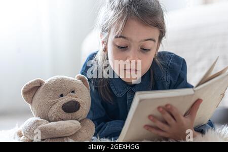 Hübsches kleines Mädchen zu Hause, das mit ihrem Lieblingsspielzeug auf dem Boden liegt und Buch liest. Stockfoto