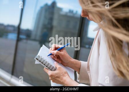 Überarbeitete Geschäftsfrau. Multitasking-Geschäftsfrau, die mit einem Mobiltelefon in einer leichten Jacke in der Nähe eines Bürogebäudes spricht. Kaukasische Frau Stockfoto