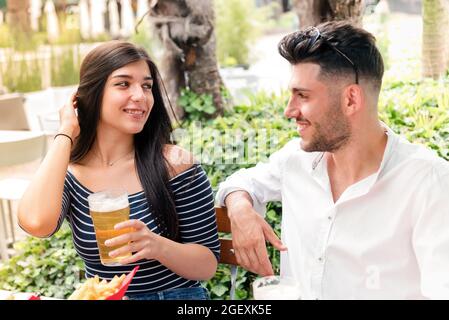 Attraktive junge Frau, die mit einem Mann bei einem Bier in einem Restaurant oder Pub im Freien flirtet, während sie ein romantisches Date genießen, das sich gegenseitig in die Augen lächelt Stockfoto