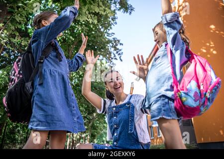 Eine junge Frau unterstützt die Töchter moralisch mit Händen ermutigt die Kinder, Mutter begleitet die Schüler zur Schule. Stockfoto